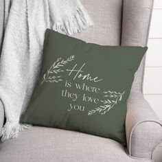 a green pillow with the words home is where they love you on it next to a gray chair