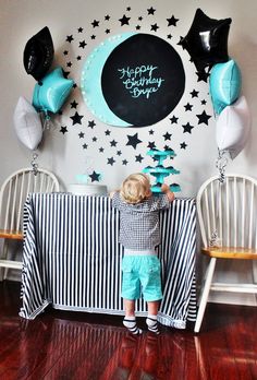 a little boy standing in front of a table with black and white balloons on it