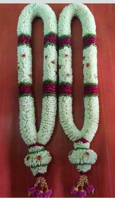 two flower garlands with bells hanging from the side on a wooden floor in front of a red wall