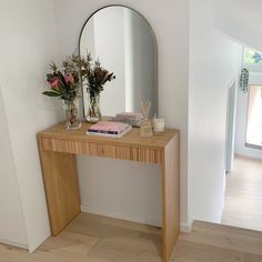 a wooden table topped with a mirror and vase filled with flowers