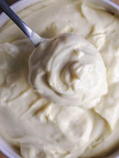 a white bowl filled with cream on top of a wooden table next to a spoon