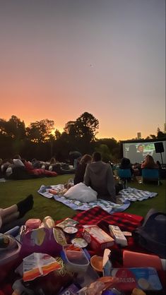 people are sitting on blankets in the grass watching tv and eating food at sunset or dawn