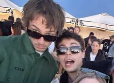 two young men standing next to each other in front of a group of people wearing sunglasses