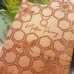 a wooden cutting board with bees and honeycombs engraved on the side, sitting in front of a potted plant