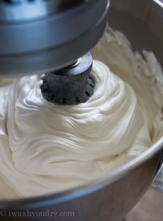 a mixer filled with white frosting in a metal bowl on top of a counter