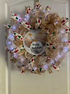 a christmas wreath on the front door decorated with holiday lights and ribboned around it that says happy holidays