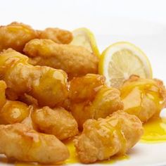 some fried food on a white plate with lemon wedges