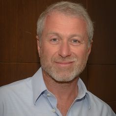 a man in a blue shirt smiling at the camera with wood paneling behind him