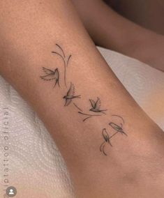 a small tattoo on the leg of a woman with birds flying above it and flowers in the air