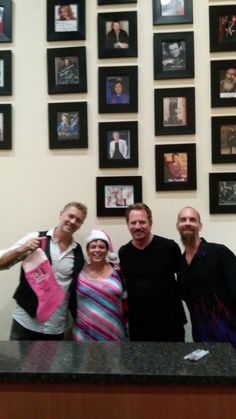 three men and a woman standing in front of a counter with pictures on the wall