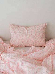 an unmade bed with pink sheets and pillows on top of it in front of a white wall