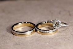 two wedding rings sitting on top of each other in front of a stone floor with white and gold accents