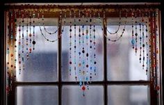 a window with beads hanging from it's side and a cat sitting in the window sill