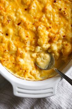 a white casserole dish filled with macaroni and cheese, topped with a spoon