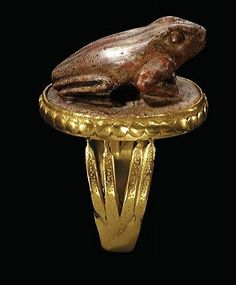 a gold ring with a frog sitting on it's side, against a black background