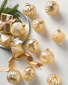 gold christmas ornaments on a white tablecloth with ribbon and gift box next to them