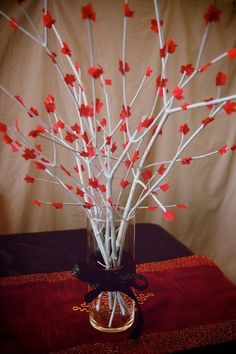 a vase filled with branches and red flowers on top of a brown tablecloth covered table