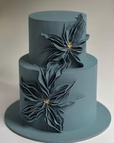 a three tiered blue cake with large flowers on the top and sides, sitting on a white table