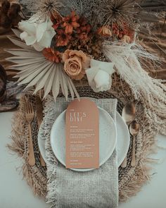 a place setting with an orange menu card and silverware on the plate, surrounded by dried flowers