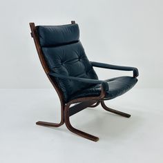 a black leather chair sitting on top of a white floor next to a wooden frame