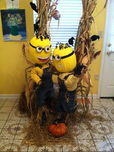 two yellow minion dolls sitting on top of hay next to pumpkins and corn stalks