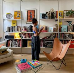 a woman standing in front of a bookshelf filled with lots of books next to a chair