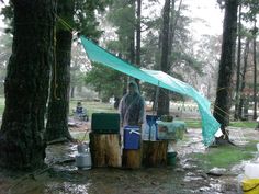 a man standing in the rain next to a tent and some trash cans under trees