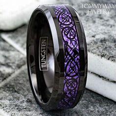 a purple and black wedding ring with an intricate design on the inside is sitting on concrete