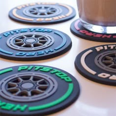 four black and green coasters sitting on top of a white table next to a cup