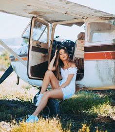 a woman sitting on the ground next to an old plane with its door open and her legs propped up