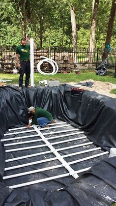 two men working on an inflatable pool with black tarp and white piping