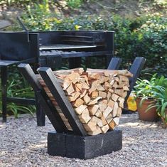 a pile of firewood sitting in front of a black bbq grill on gravel