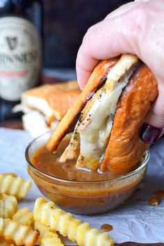 a person is dipping some food into a small glass bowl with french fries on the side