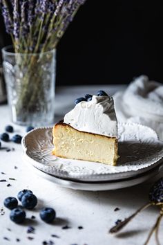 a piece of cake sitting on top of a white plate next to a vase with blueberries