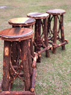 three wooden stools made out of logs on the grass in front of some trees