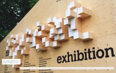 an exhibition sign is displayed on the side of a building in front of some trees