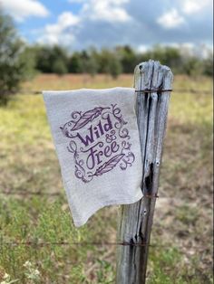 a tea towel hanging on a fence post in the middle of a field with wild tree written on it