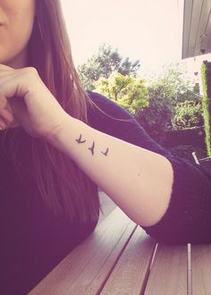 a woman with a bird tattoo on her arm sitting at a wooden table outside in the sun