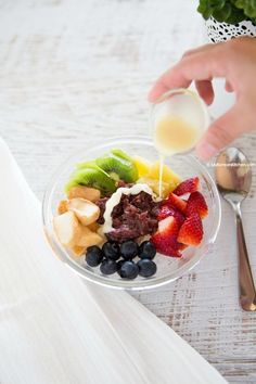 a person pouring milk on top of a bowl of fruit and vegtables