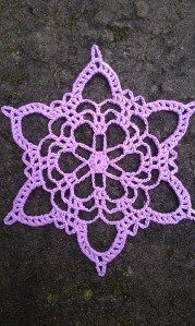 a purple crocheted doily laying on the ground