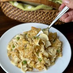 a person is holding a fork over a plate of pasta with peas and cheese on it