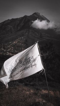 a white flag on top of a mountain with clouds in the sky and mountains behind it