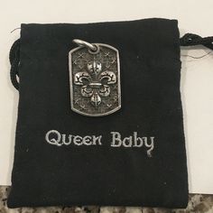 a black bag with a silver dog tag on it and the words queen baby written in white