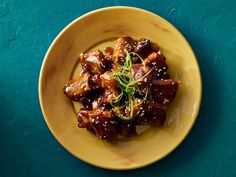 a yellow plate topped with meat covered in sauce and garnished with green herbs