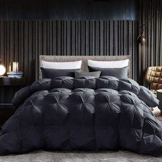 a bed with black comforter and pillows in a room next to a lamp on a table