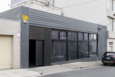 a black car parked in front of a building on the side of a street with garage doors open