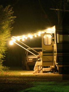 a camper parked in the dark with lights strung from it's roof and door