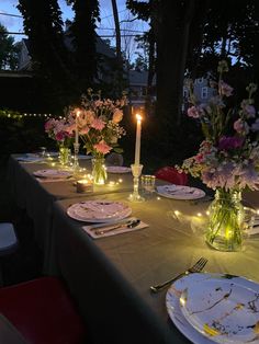 the table is set with plates, candles and flowers in glass vases on it