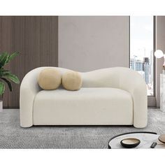 a white couch with two pillows on it in front of a potted plant and table