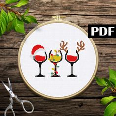 a cross stitch pattern with two wine glasses and santa's hat on it next to scissors